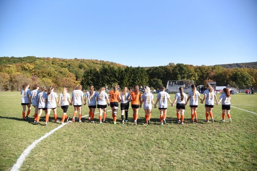 The girls varsity soccer team walking across the soccer field hand-in-hand.