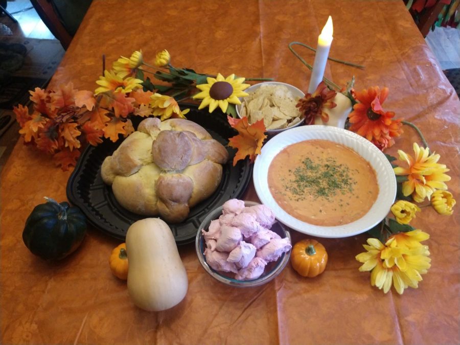 A plate of Pan de Muertos, a bowl od divinity and a saucer of salsa dip wreathed with fall foliage.
