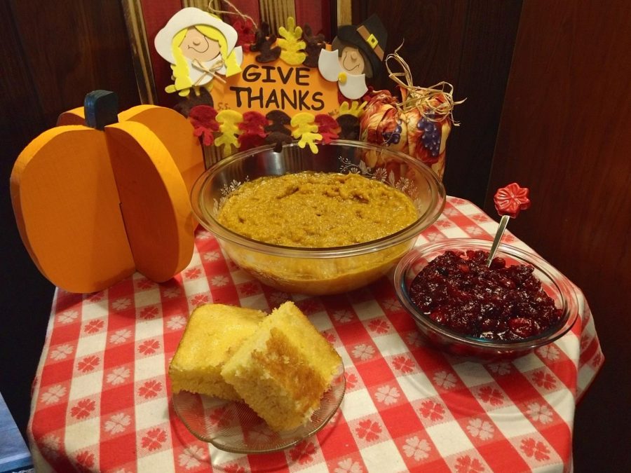 A plate of cut cornbread, a bowl of cranberry sauce and a floral decorated bowl of butternut squash decorated appropriate to the season.