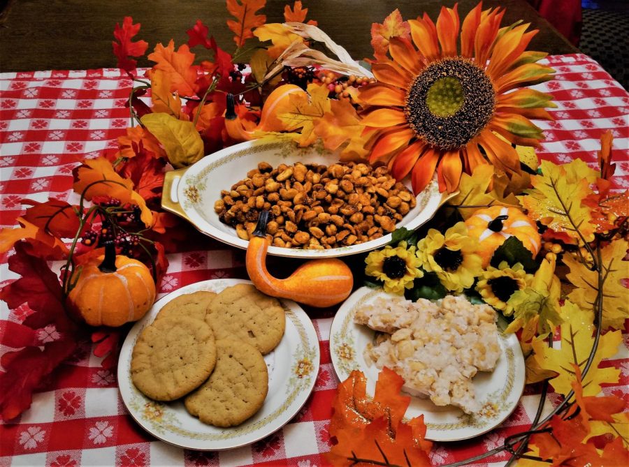A bowl of honey roasted peanuts preceding plates of peanut butter cookies and peanut brittle enwreathed in seasonal flora.