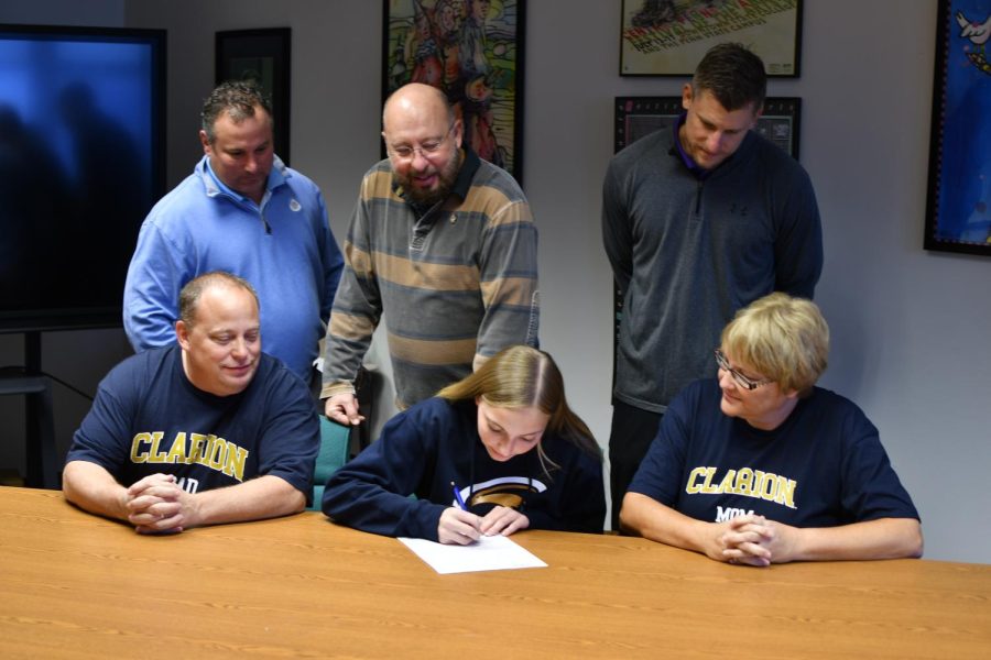 Latchford signs her letter of intent as her father Bill Latchford, mother Jenny Latchford, TAHS Athletic Director Luke Rhoades, TAHS principal Tom Yoder and TAHS Track and Field Head Coach Brad Kanuch look on.