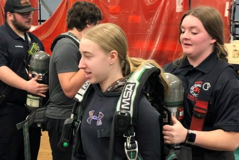 Neptune junior firefighter Rayann Walls (right) helps Tyrone student Nora Hoy gear up at a recent firefighting demonstration. 